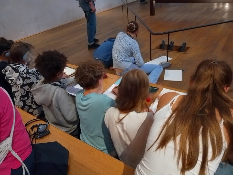 Blick von hinten auf einige Schüler:innen, die auf einer Kirchenbank sitzen